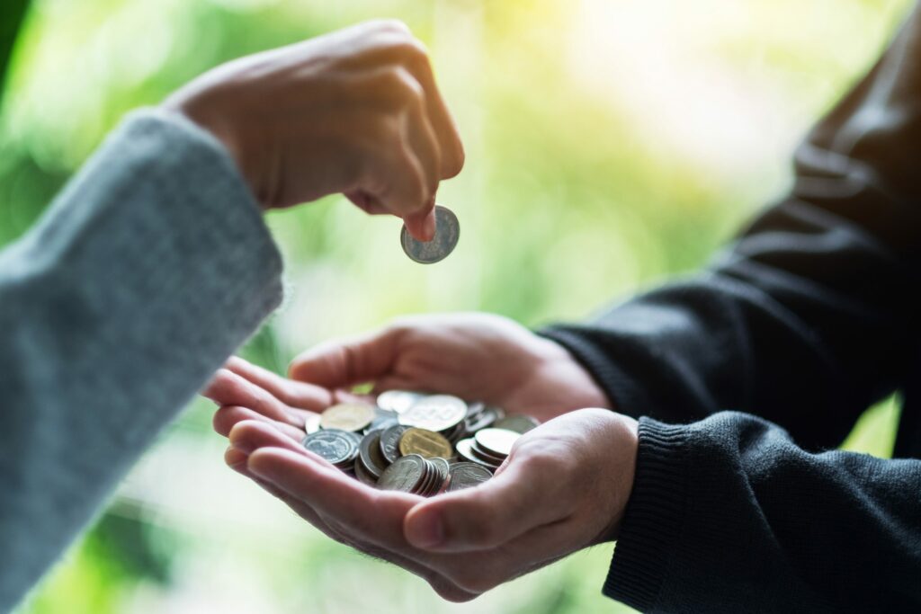 A hand dropping a coin into open palmed hands containing other coins