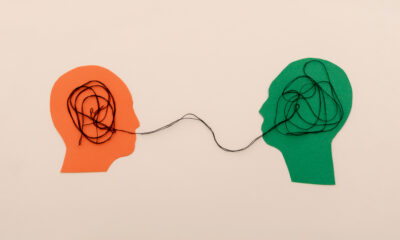 Two paper-cut head silhouettes in orange and green connected by a tangled thread